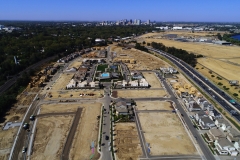aerial view of a development site with lots at various stages of construction and a view of tall buildings in the background